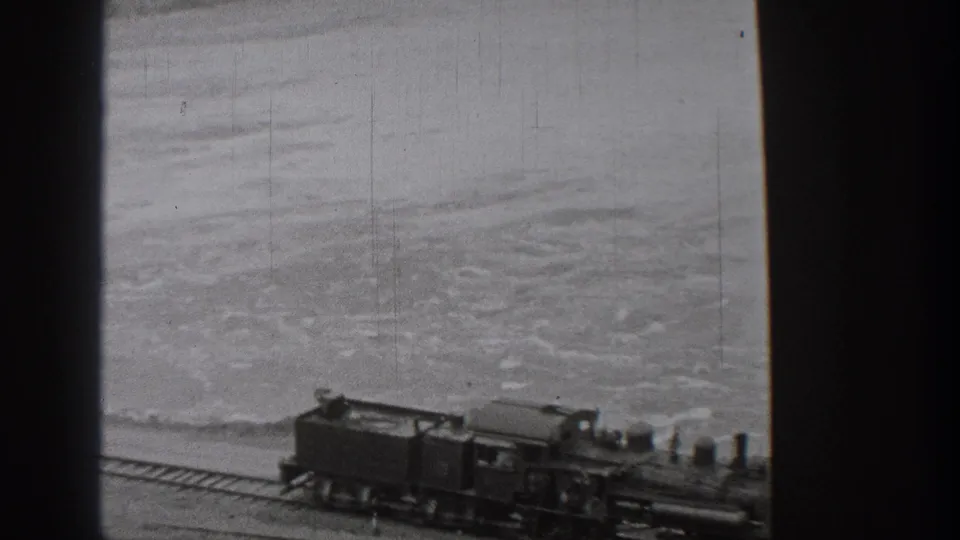 Riverside view of a steam train and tender on Washington tracks in 1938, with water and shoreline behind the rail line.