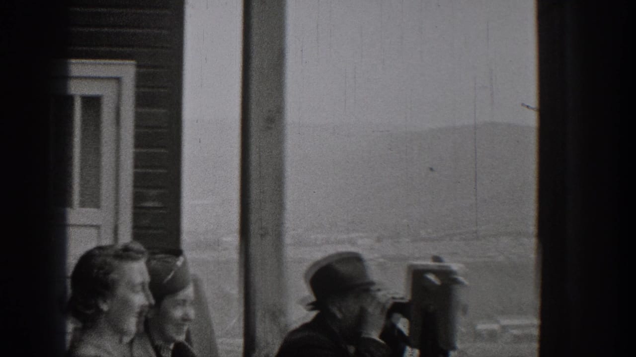 Adults stand near a building and a coin-operated binocular viewer.
