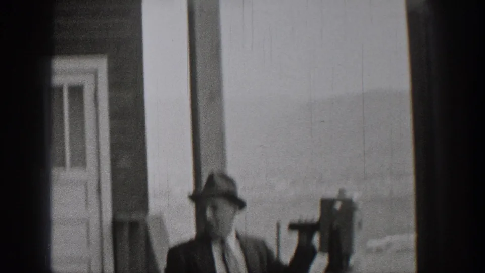 Adult man in period dress stands near a coin-operated viewer at a Washington scenic overlook, with a doorway and hazy background visible.