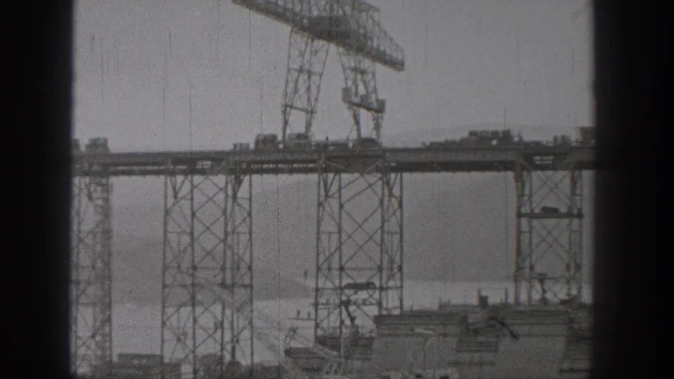 1938 Washington 8mm frame showing tall steel cranes and elevated bridge construction over a broad river.
