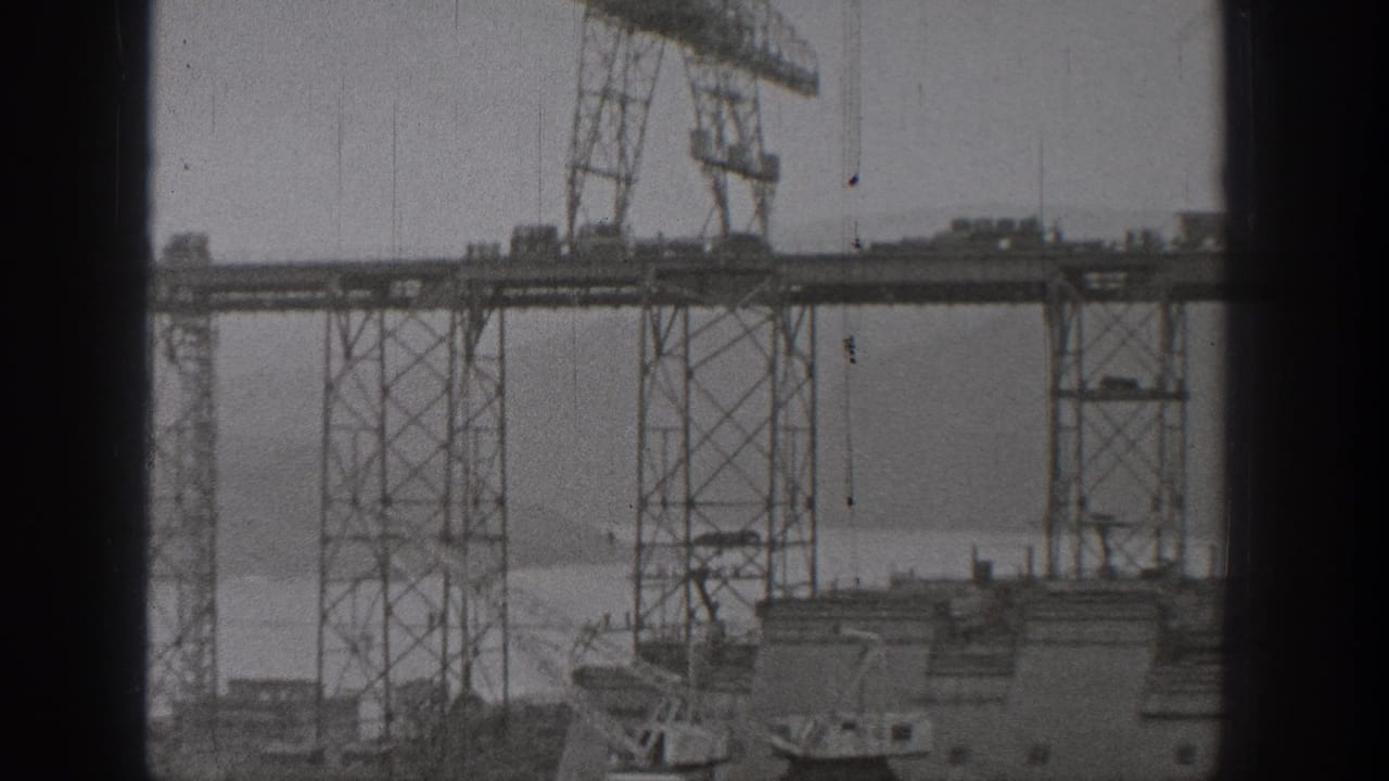 Home-movie view of bridge or waterworks construction in Washington, with cranes set along high steel spans over water.