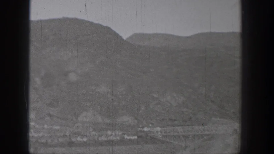 1938 Washington 8mm frame showing misty foothills above a small valley settlement, with archival scratches and gate edge visible.