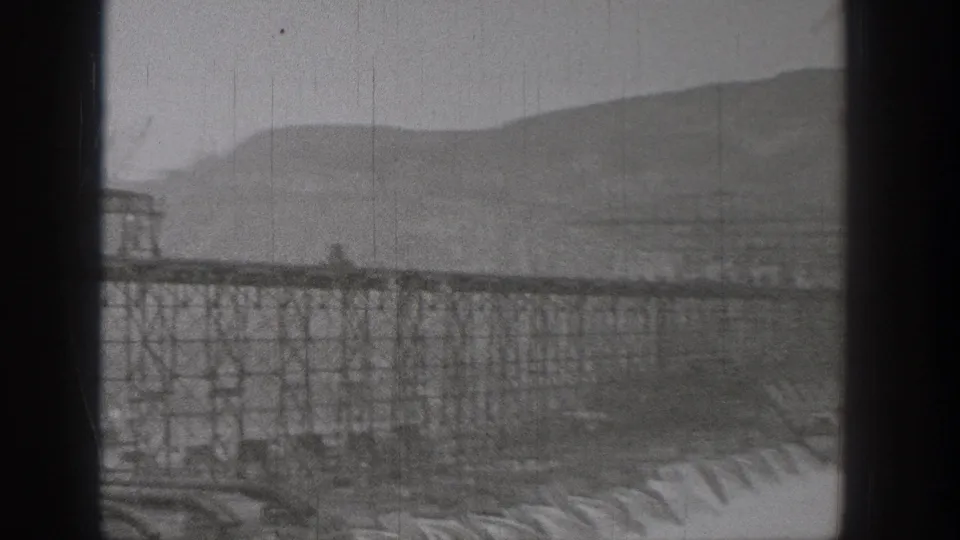 1938 Washington view of a dam-area structure, water below, and mountain ridges beyond.