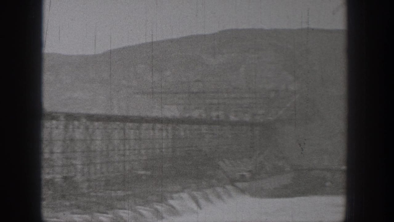 1938 Washington 8mm frame showing a distant industrial trestle or bridge, possible channel below, hills behind, and dark camera-frame borders.