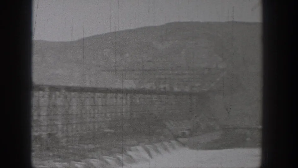 1938 Washington 8mm frame showing a distant industrial trestle or bridge, possible channel below, hills behind, and dark camera-frame borders.