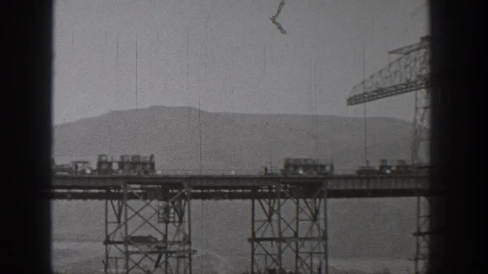 1938 Washington frame with small rail carts on an elevated steel bridge or trestle, a crane at right, and mountains in the background.