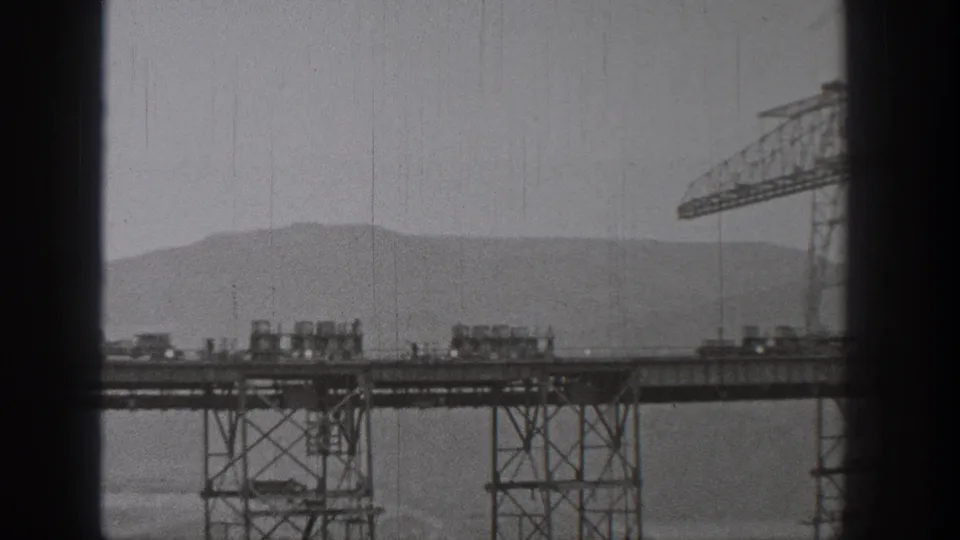 1938 Washington 8mm view of carts on a raised steel structure, with a crane partly visible and dry hills behind.