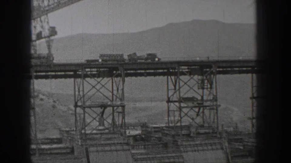 1938 Washington frame showing a closer section of the elevated steel trestle, small carts on the deck, a crane, and hills in the distance.