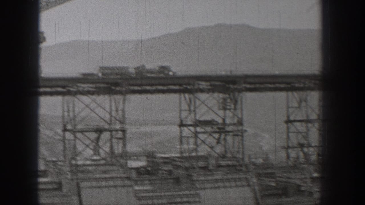1938 Washington 8mm frame showing distant bridge or dam construction with steel supports, work platforms, mist, and mountain silhouettes.
