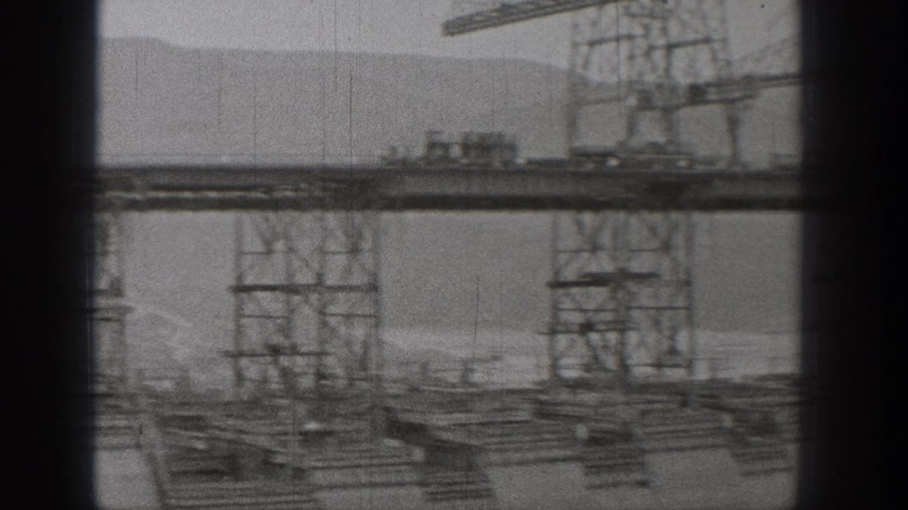 Crane and elevated construction track above a large industrial structure near water or mist.