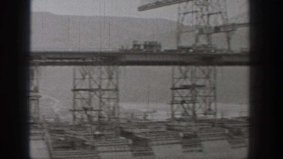 1938 Washington construction view with a crane boom, elevated track or platform, steel towers, and soft mountainous background.