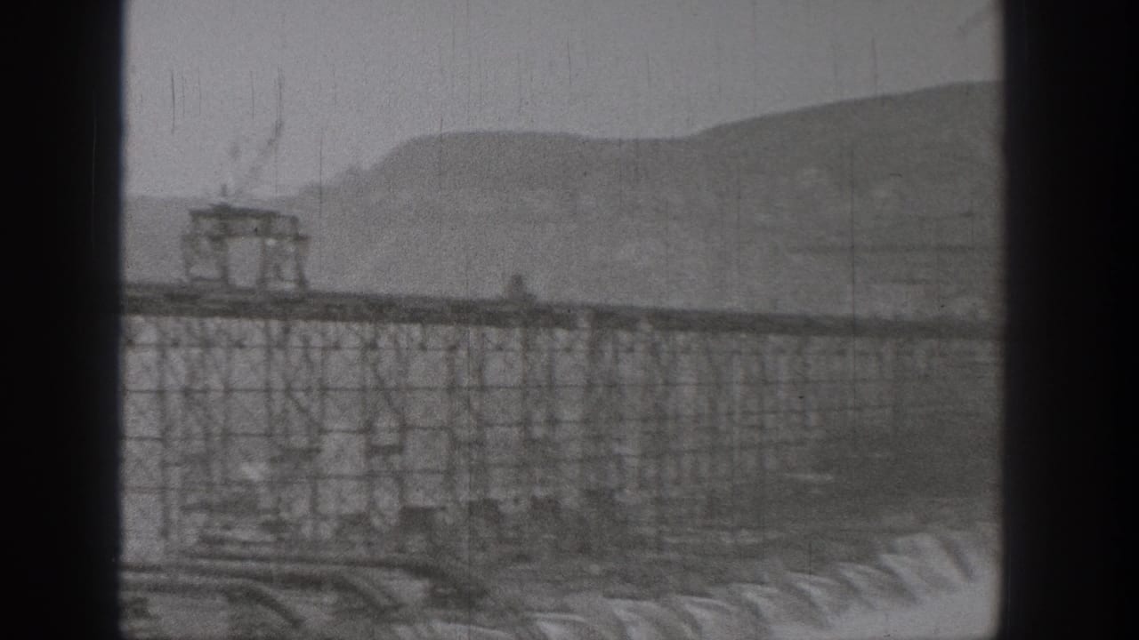 1938 Washington footage appears to show Grand Coulee Dam construction through dark foreground framing, with scaffolding, concrete forms, and hills.