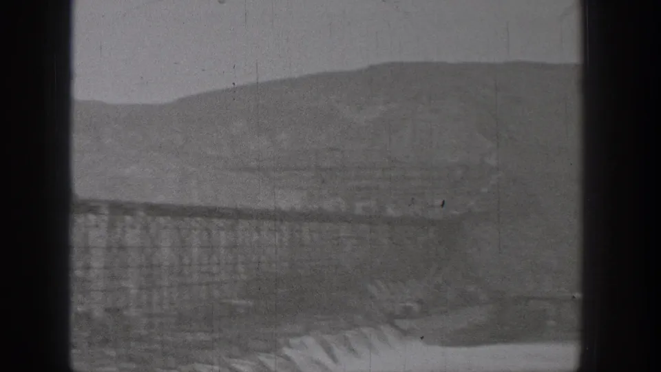 Grand Coulee Dam construction in Washington, with broad concrete sections, scaffolding, and rugged hills visible in black-and-white 8mm footage.