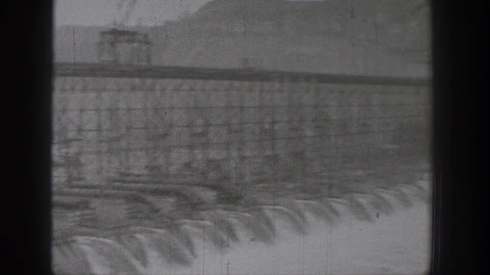 Washington dam footage showing concrete spillway water and a distant industrial crossing softened by exposure and film wear.