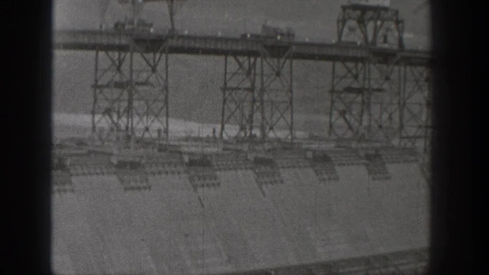 1938 Washington dam view with a metal truss crossing, support towers, concrete spillway, and water visible below.