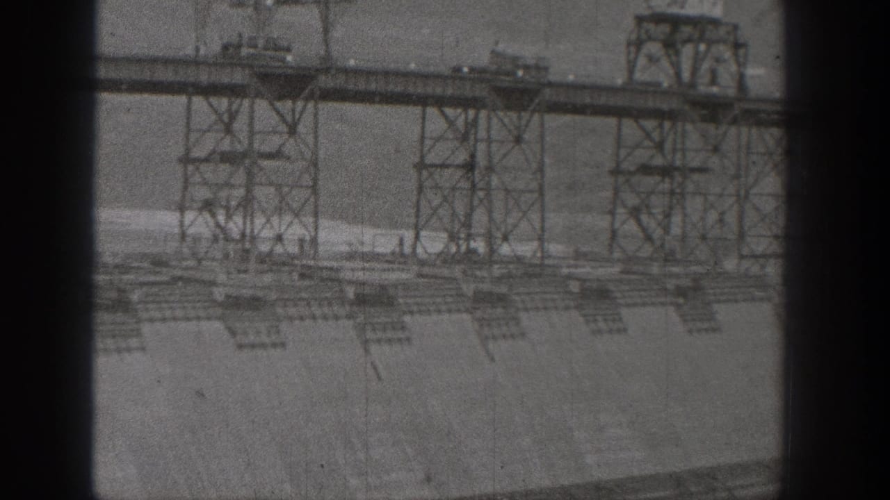1938 Washington home-movie view of a hydroelectric dam face with steel construction towers and heavy black film-gate borders.