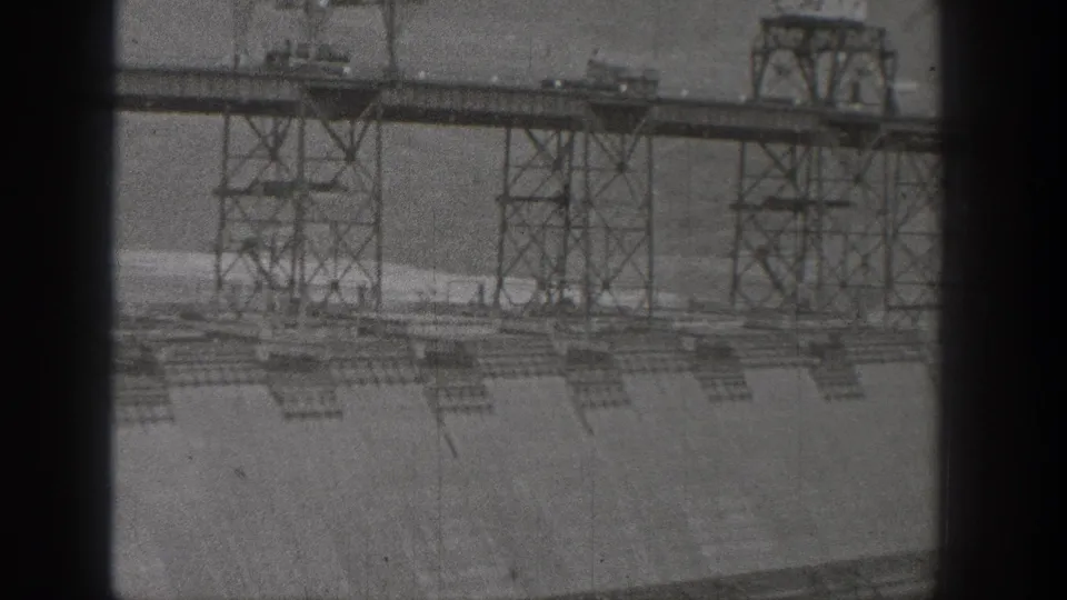 1938 Washington home-movie view of a hydroelectric dam face with steel construction towers and heavy black film-gate borders.