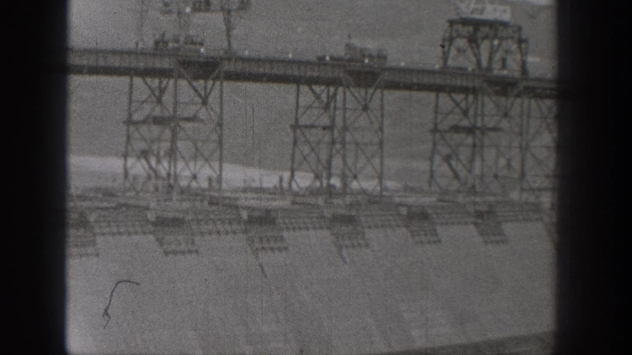 Black-and-white 8mm frame of the Washington hydroelectric dam construction, with steel trestles over a broad concrete surface.