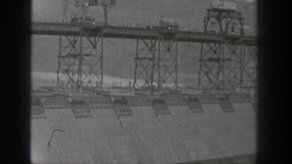 Black-and-white 8mm frame of the Washington hydroelectric dam construction, with steel trestles over a broad concrete surface.
