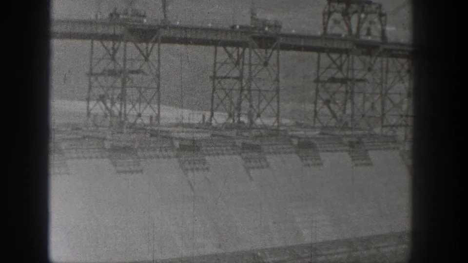 1938 Washington 8mm view of the dam wall and overhead steel structures, softened by grain, scratches, and film-gate shadows.