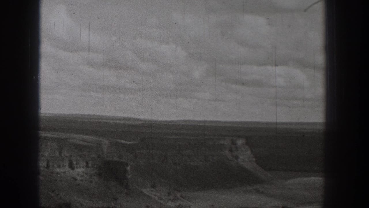 1938 Washington 8mm frame showing open arid ground, eroded slopes, and a distant dirt route under a cloudy sky.