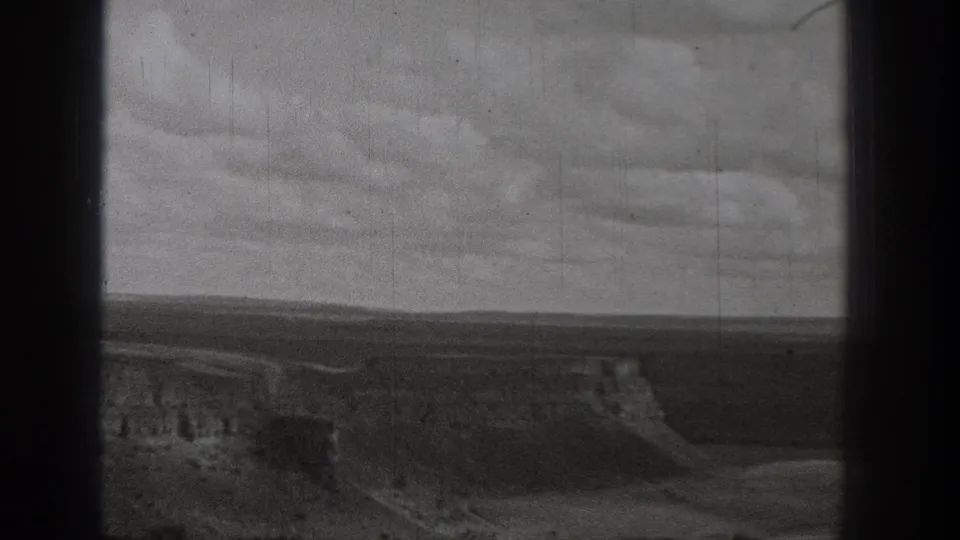 1938 Washington 8mm frame showing open arid ground, eroded slopes, and a distant dirt route under a cloudy sky.