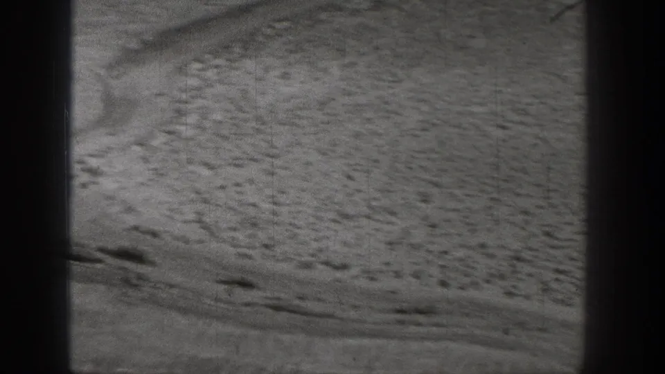 Black-and-white 1938 Washington frame showing sandy desert surface, sparse scrub, scattered stones, and a faint track.