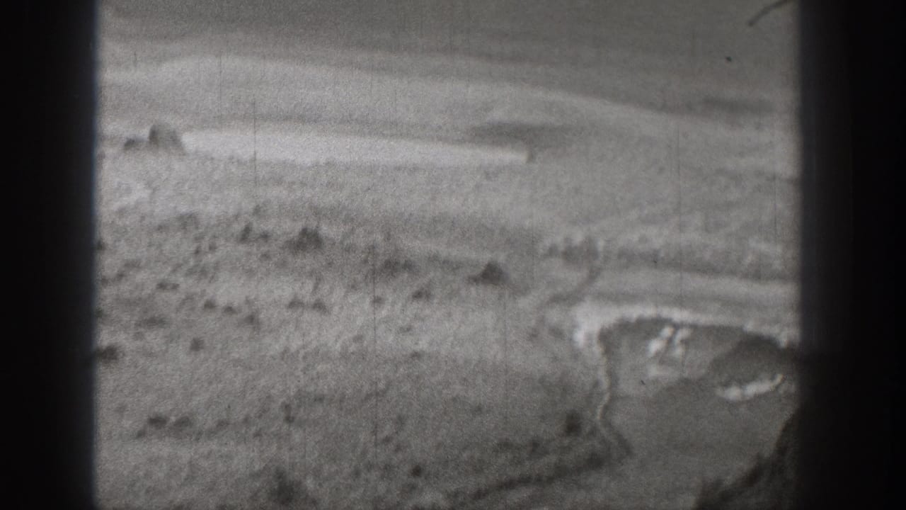 1938 Washington home-movie frame showing an arid landscape with pale ground, low hills, and a curved pool or shoreline.