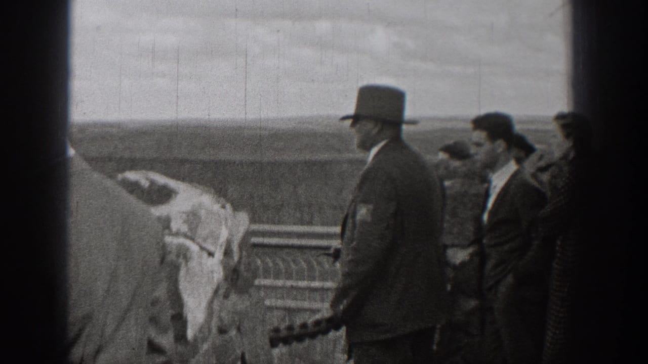 1938 Washington home-movie frame showing adults in suits, coats, and top hats gathered near a railing at a scenic overlook.