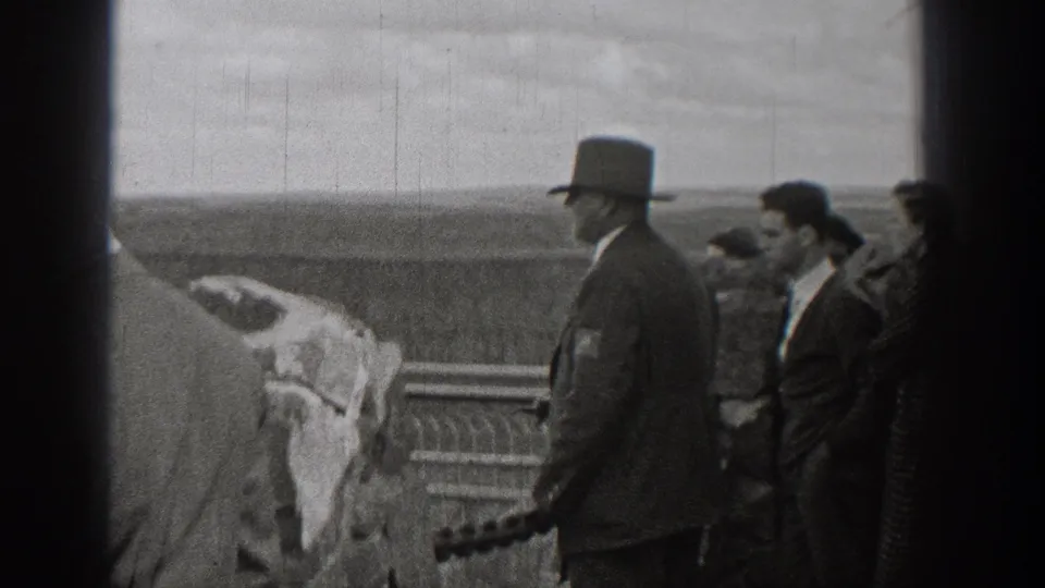 1938 Washington home-movie frame showing adults in suits, coats, and top hats gathered near a railing at a scenic overlook.