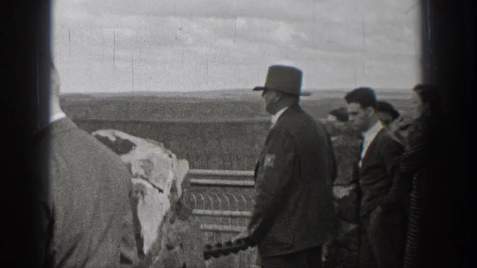 1938 Washington frame with top-hatted men and other guests beside an overlook railing, seen in grainy black-and-white 8mm footage.