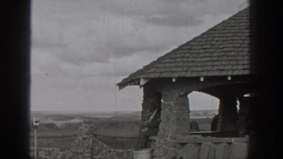 Black-and-white 8mm frame of a stone pagoda-like overlook structure in Washington, with roof detail and open landscape visible.