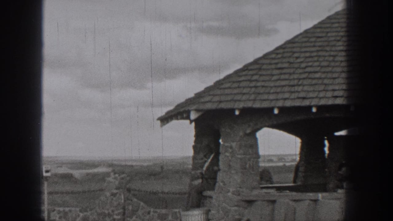 1938 Washington 8mm frame showing a stone shelter, railing, cloudy sky, and distant lake landscape.