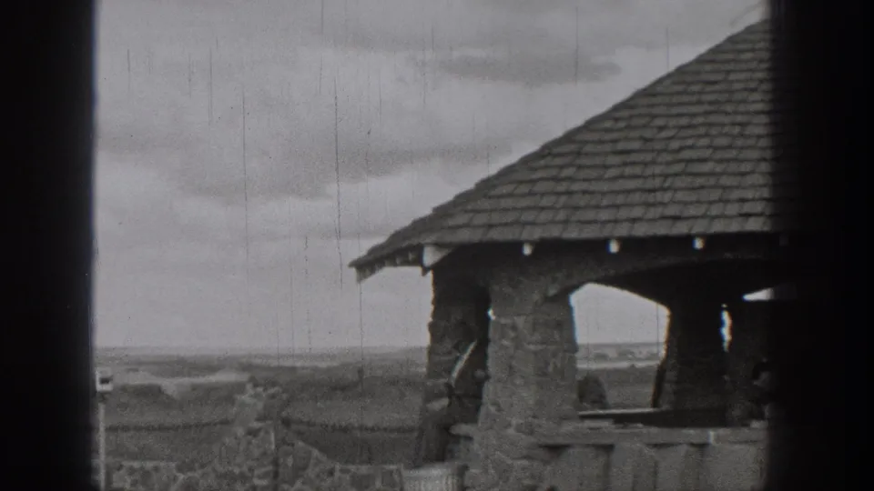 1938 Washington 8mm frame showing a stone shelter, railing, cloudy sky, and distant lake landscape.