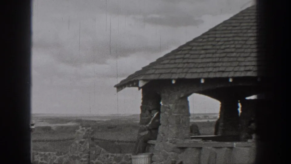 Washington home-movie frame with the stone shelter at right and distant lake country beyond.