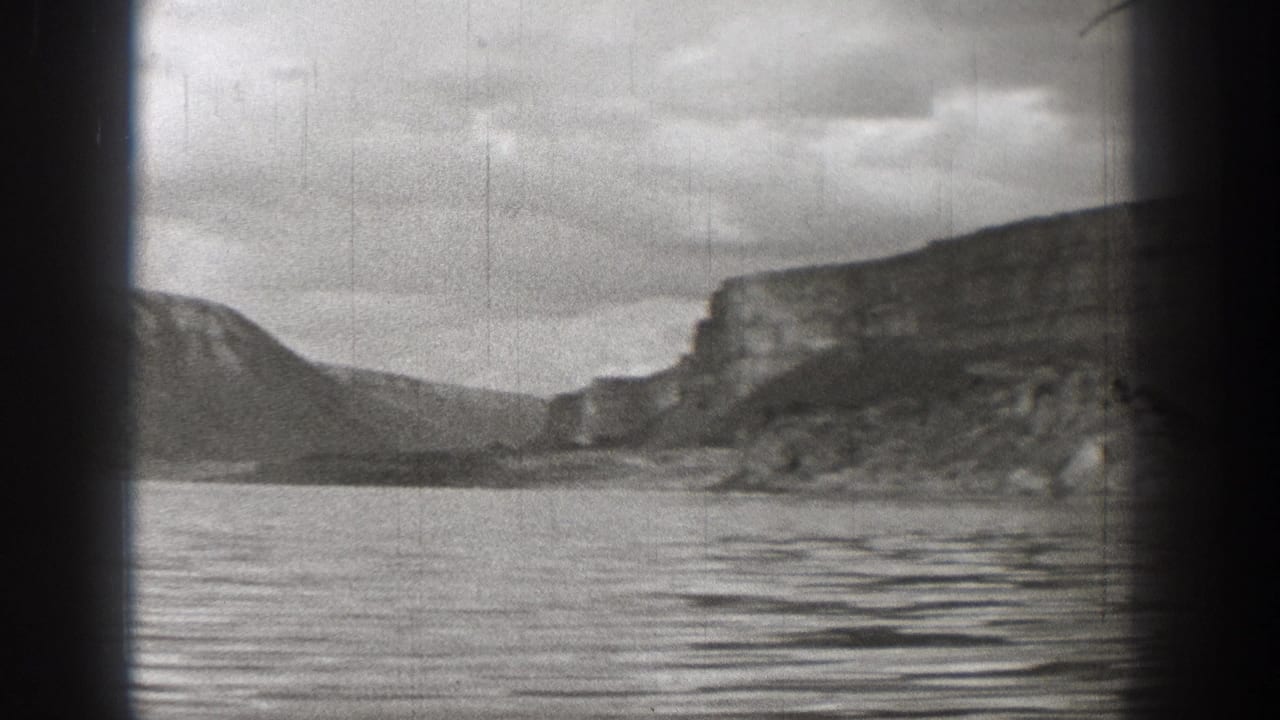 1938 Washington 8mm frame showing a still lake, rugged mountain slopes, cliff faces, and heavy black film edges.