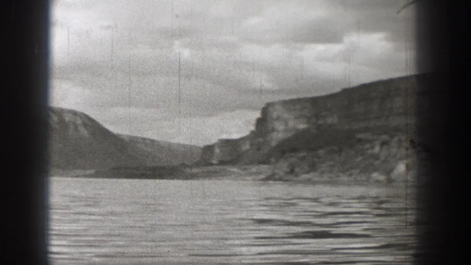 1938 Washington 8mm frame showing a still lake, rugged mountain slopes, cliff faces, and heavy black film edges.