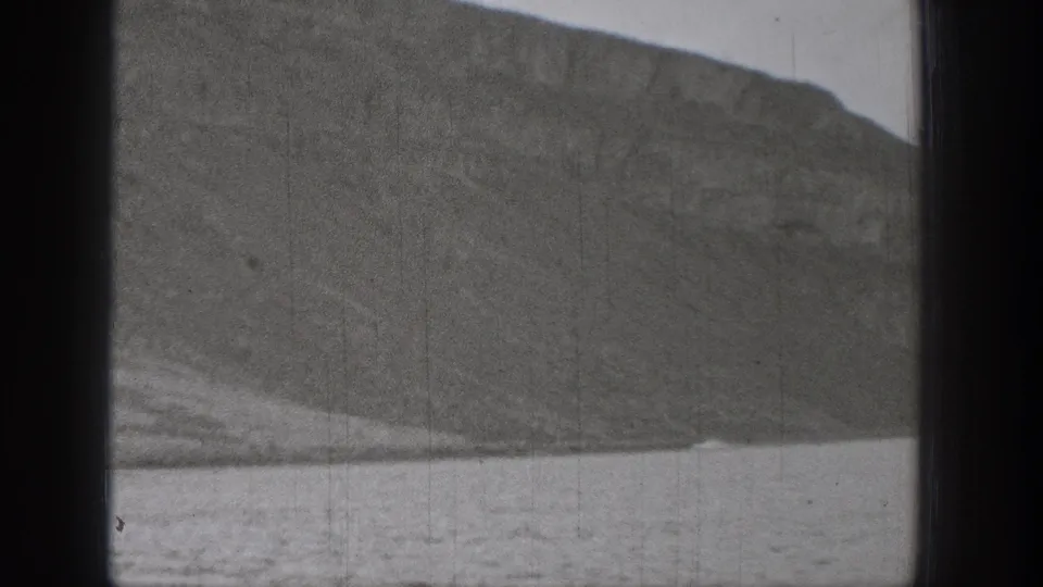 Black-and-white 1938 Washington 8mm frame showing a steep rocky slope above lake water with soft exposure and grain.