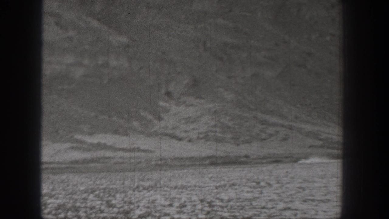 1938 Washington 8mm frame showing a small distant vehicle moving across flat desert terrain beneath rugged hills.