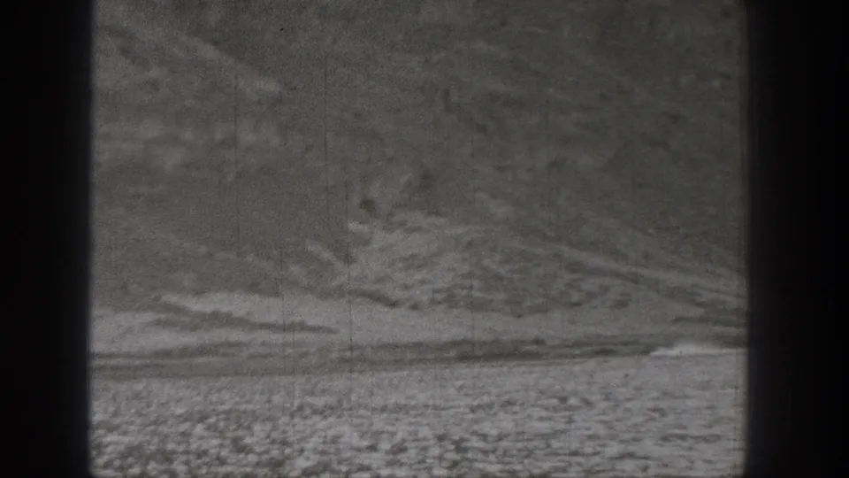 1938 Washington 8mm frame showing a small distant vehicle moving across flat desert terrain beneath rugged hills.