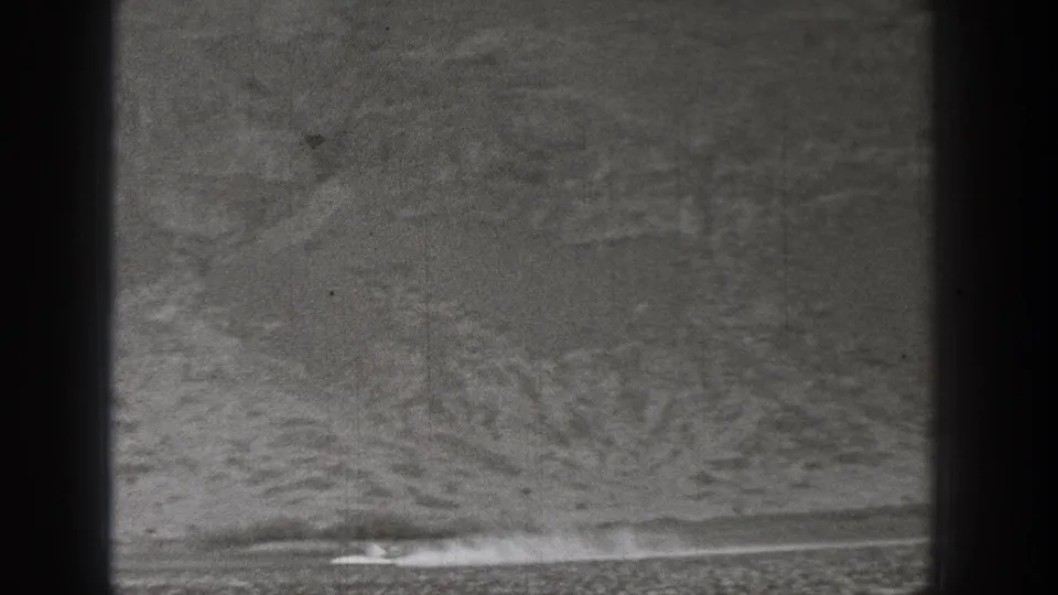 A distant 1938 Washington desert speed run shows a tiny vehicle and a long pale dust plume in 8mm film texture.