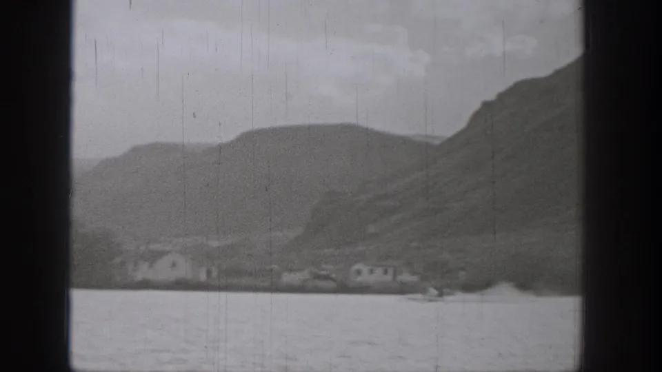1938 Washington 8mm frame showing a lake, hillside shoreline, small distant buildings, cloudy sky, and visible film gate edges.