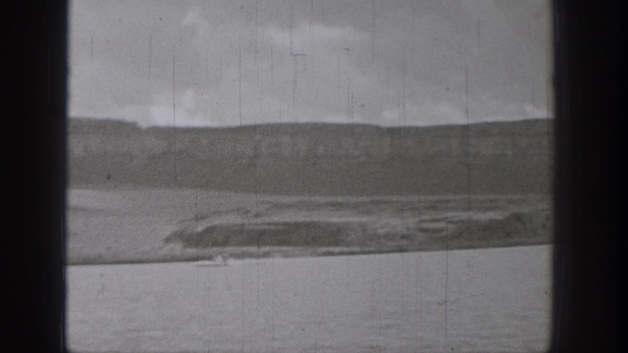 1938 Washington 8mm view across a lake toward low hills and shoreline, with a small distant boat crossing the water.