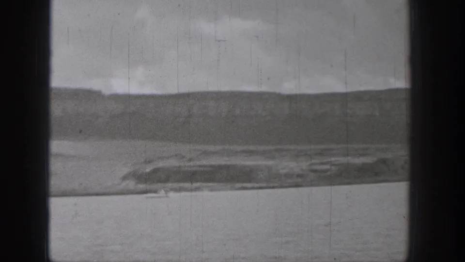 1938 Washington 8mm view across a lake toward low hills and shoreline, with a small distant boat crossing the water.