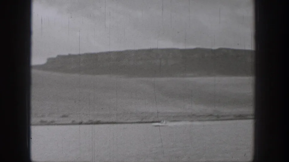 Black-and-white 8mm frame from 1938 Washington showing a broad lake, long low hill, shoreline, and small boat near the bottom of the frame.