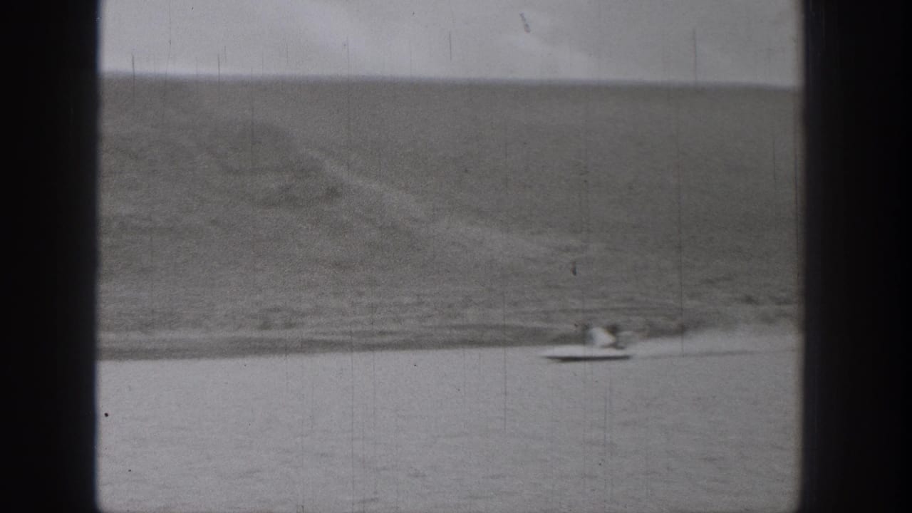 Small boat and water skier moving across a calm lake below a distant mountain slope.