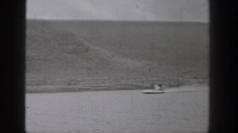 1938 Washington 8mm frame showing a small craft and possible water skier on a calm lake with a broad mountain slope behind them.