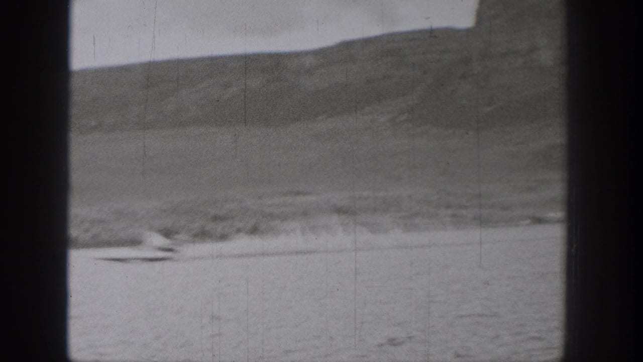 Distant 1938 Washington lake view with a small moving craft or skier leaving a wake against a soft mountainous shoreline.