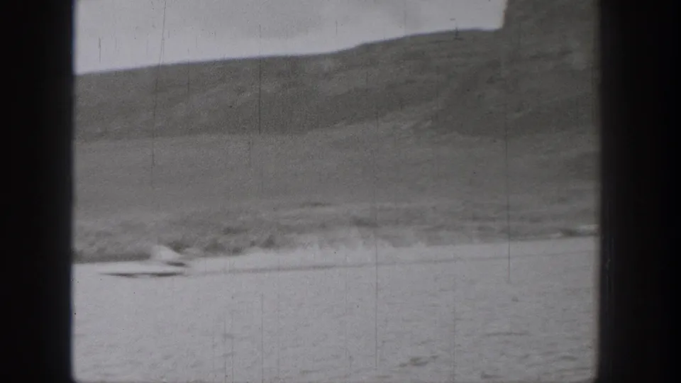 Distant 1938 Washington lake view with a small moving craft or skier leaving a wake against a soft mountainous shoreline.