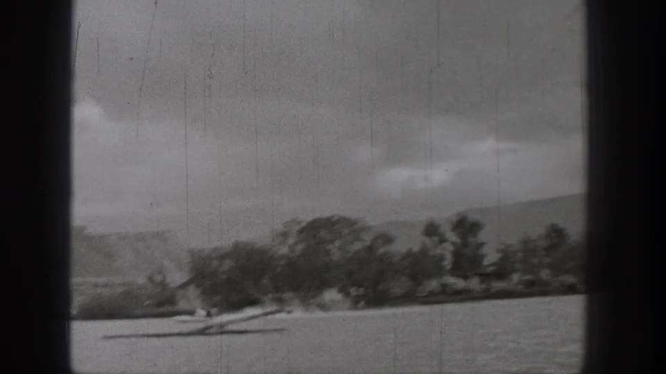 Black-and-white 1938 Washington 8mm frame showing a small boat on a lake with trees, shoreline, low hills, and overcast sky.